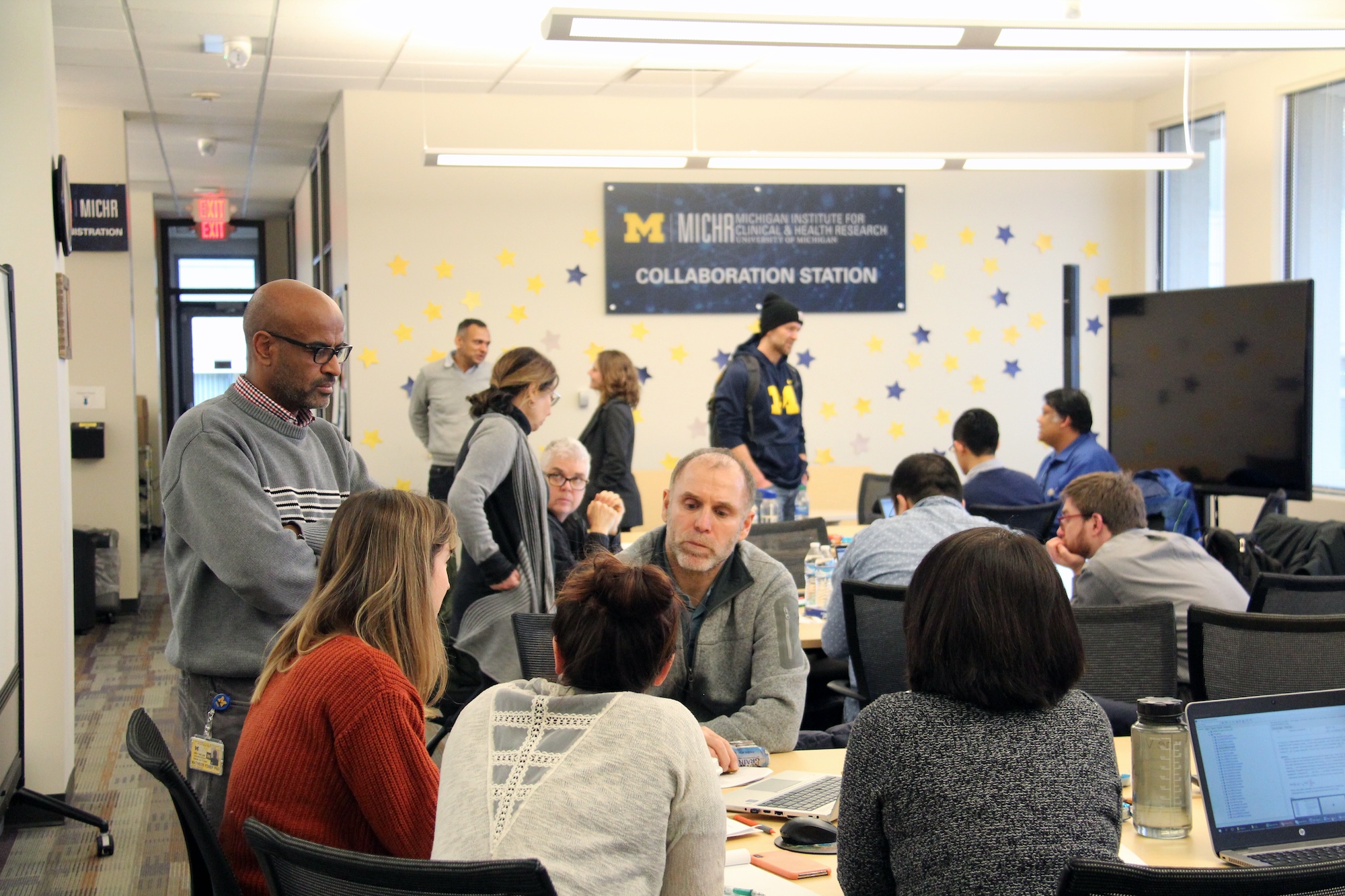 a group of people around tables working and talking